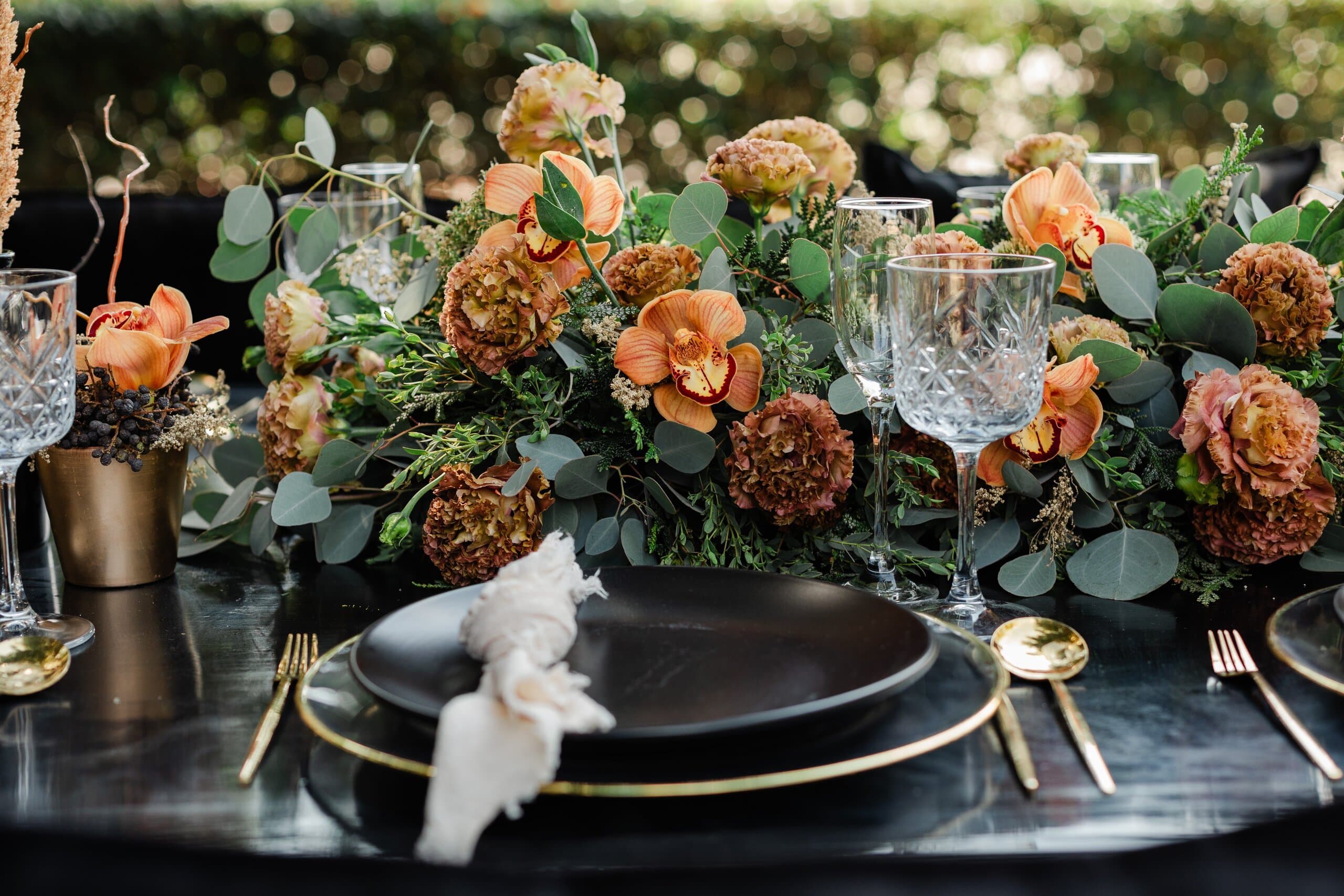 Camino de mesa con dalias, rosas en durazno y eucalipto sobre mantel negro, diseño floral de Clhei